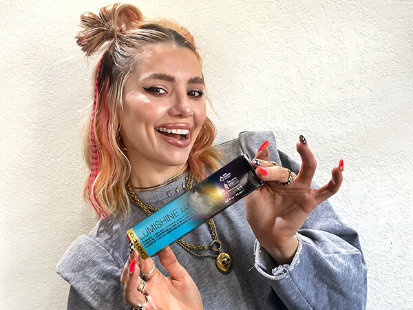 BSG_Joico_ArtistsCoverPhoto_Larisa Love Lumi10(1) Woman holding lumishine product smiling and looking at camera