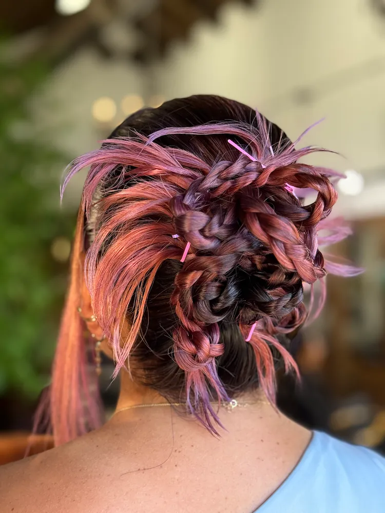 Behind the head view of woman with pink hair highlights braided into a bun